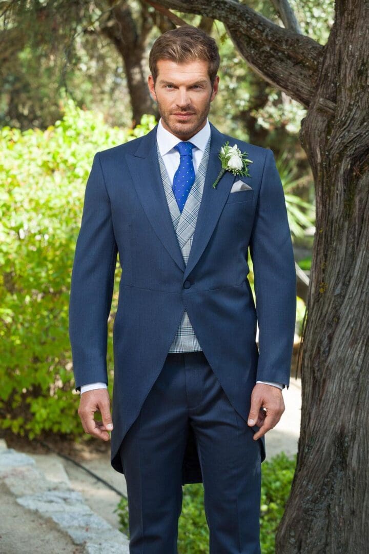 A man in a suit standing next to a tree.