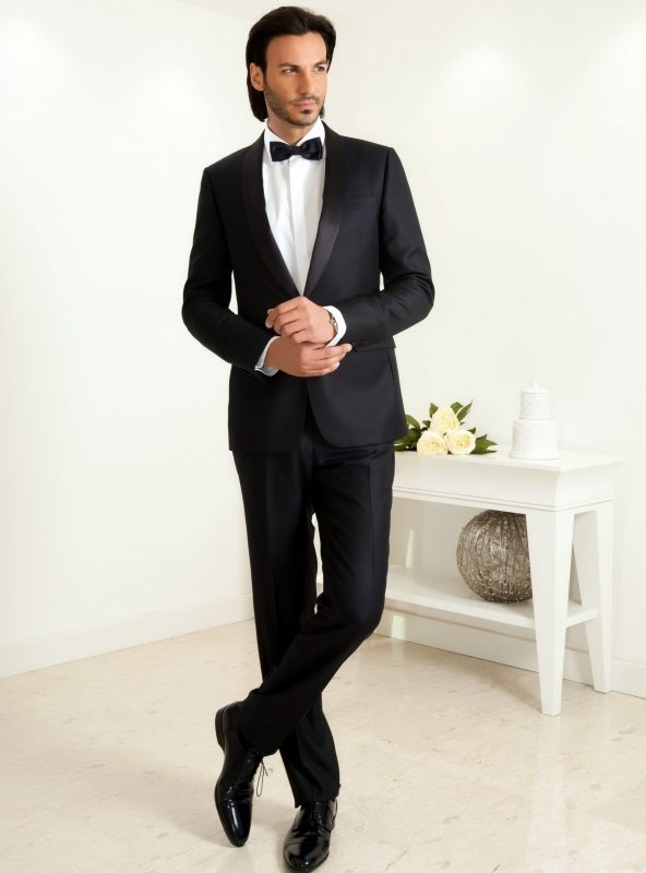 A man in a tuxedo standing next to a table.
