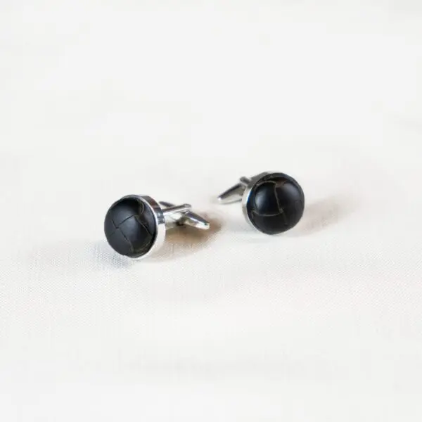 A pair of black cufflinks on top of white surface.