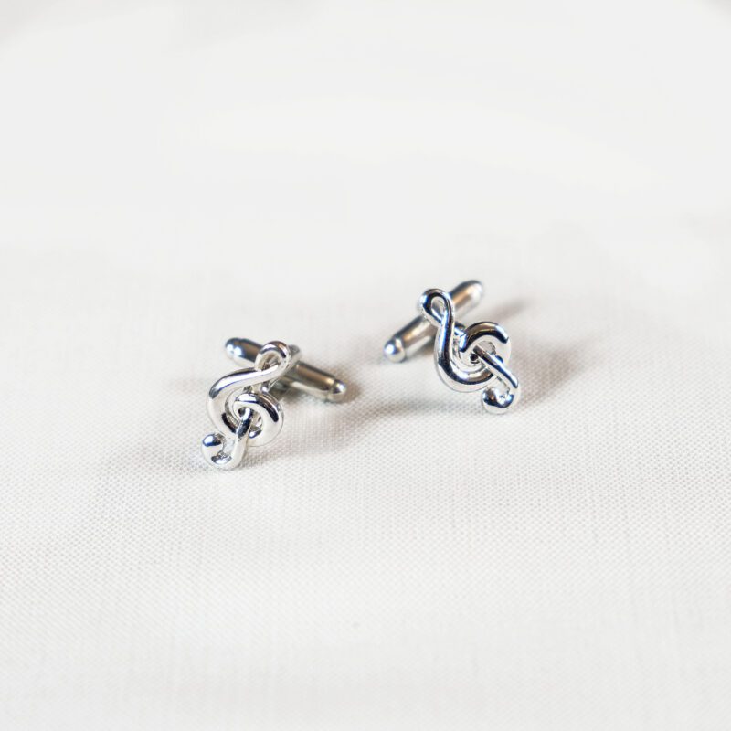 A pair of silver cufflinks with a musical note on them.