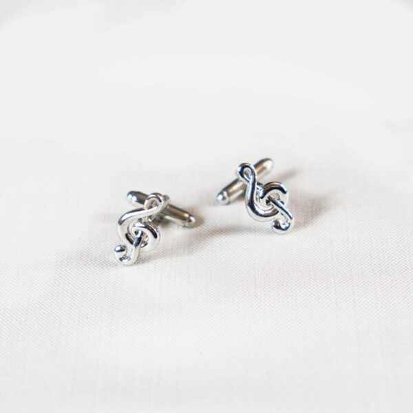 A pair of silver cufflinks with a treble clef on top.