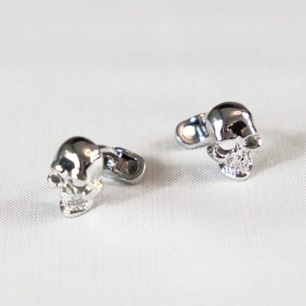 A pair of silver skull earrings sitting on top of a table.