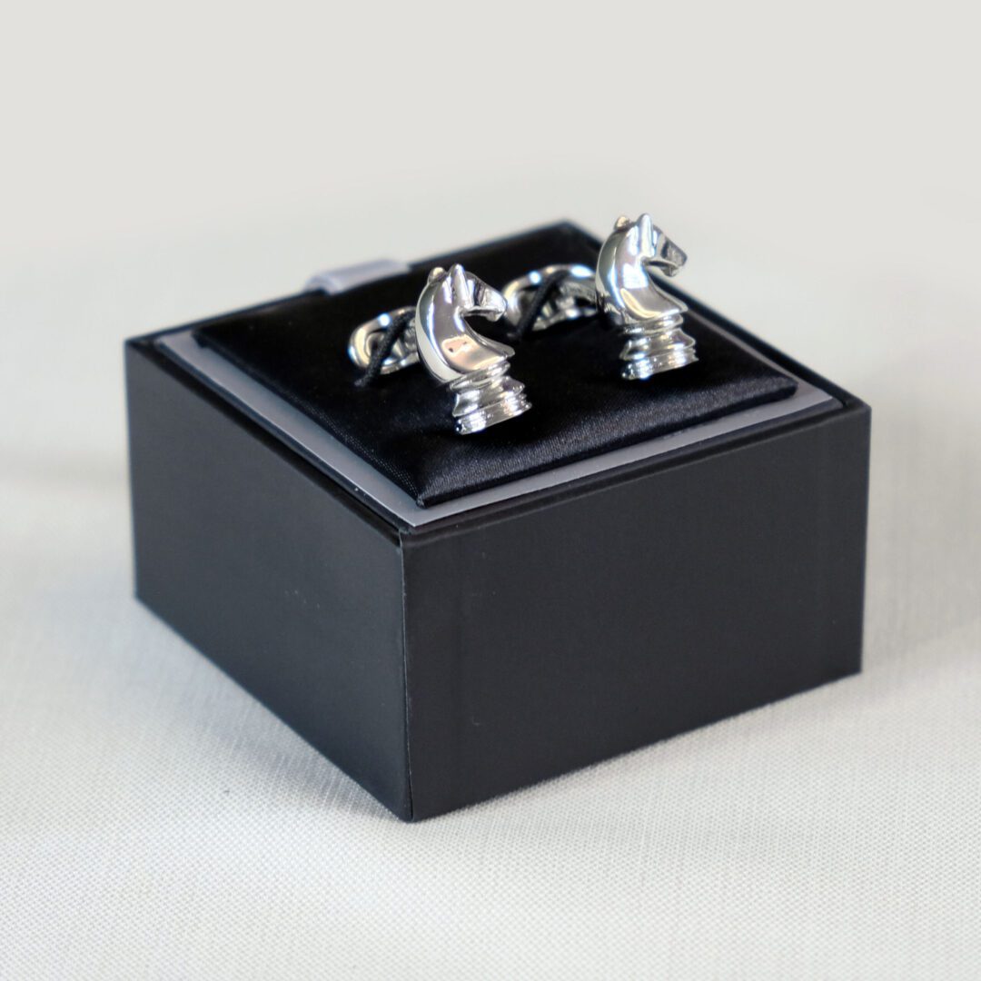 A black box with two silver cufflinks on top of it.