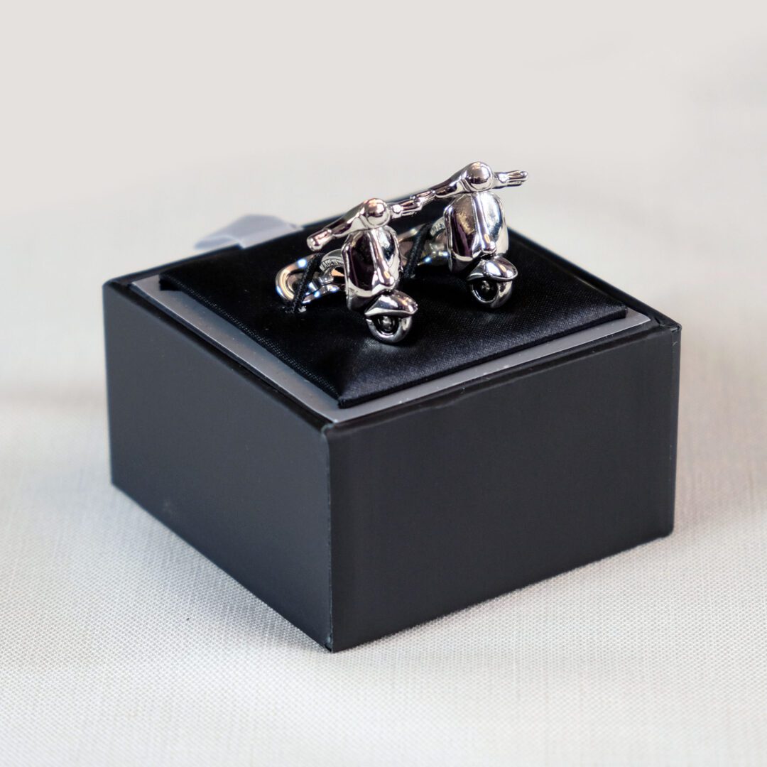 A black box with two silver cufflinks on top of it.