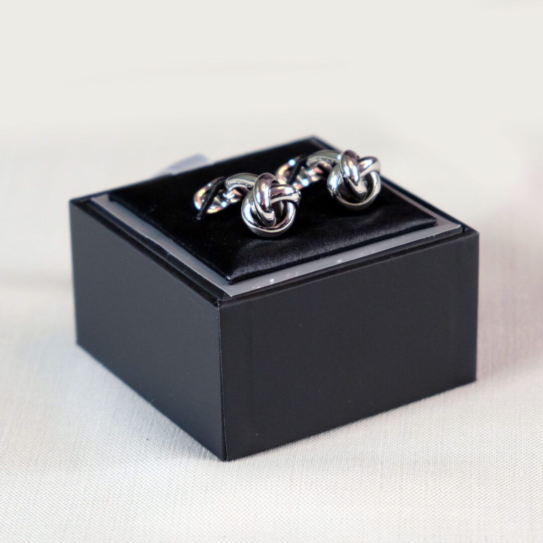 A black box with two silver cufflinks on top of it.