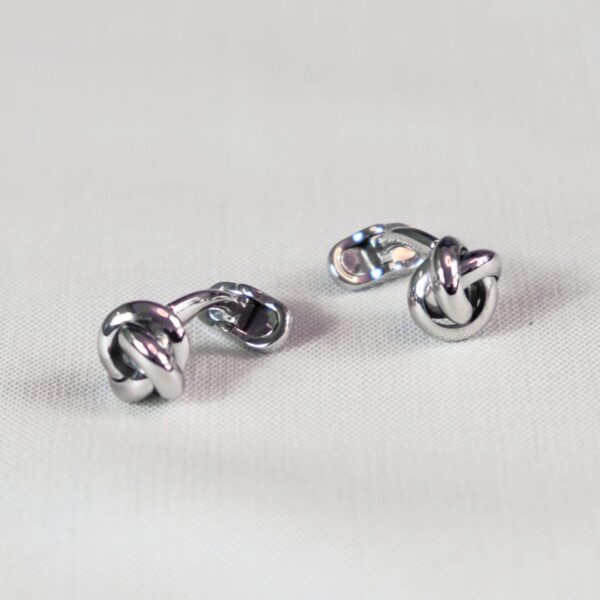 A pair of silver knot cufflinks on top of a table.