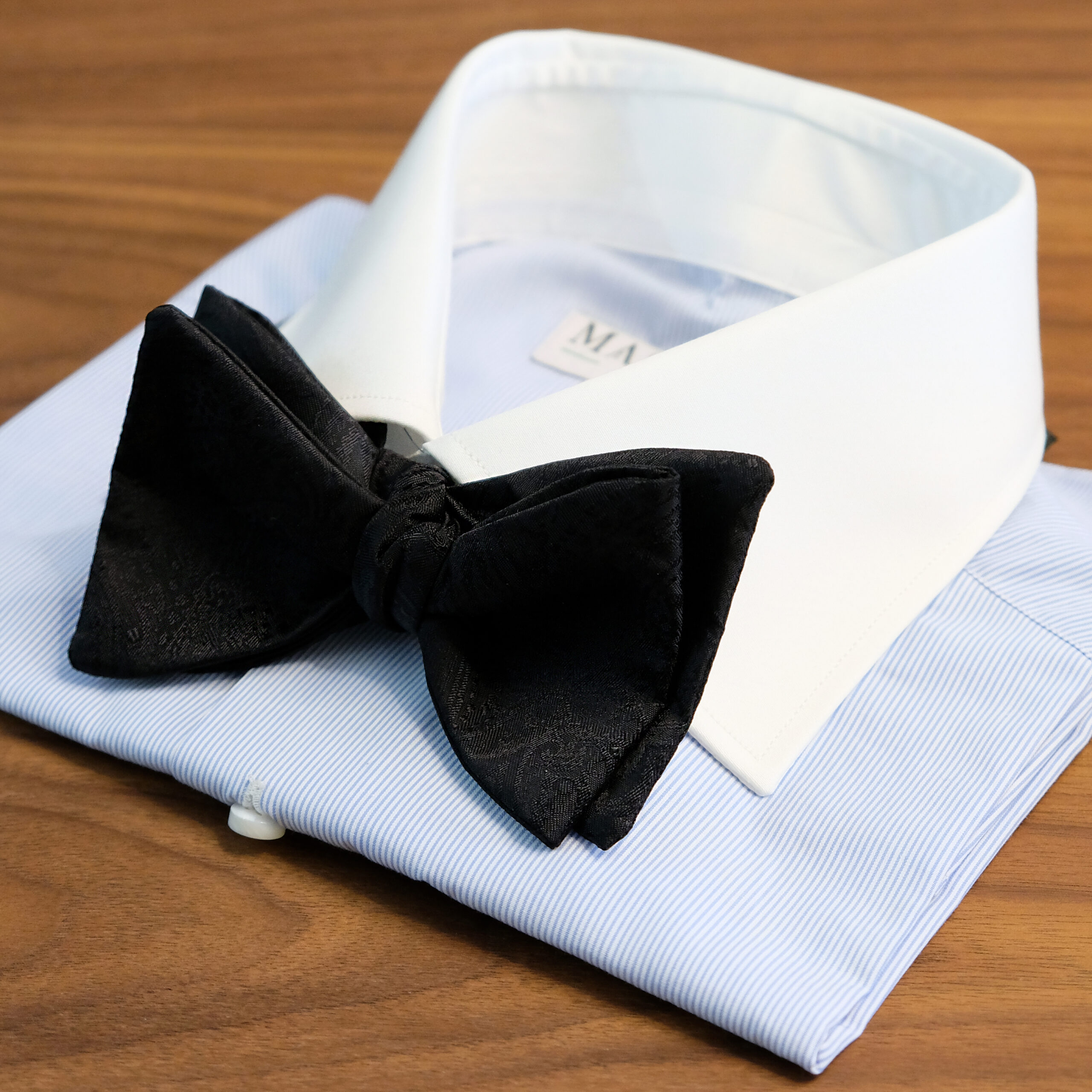 A black bow tie on top of a white shirt.