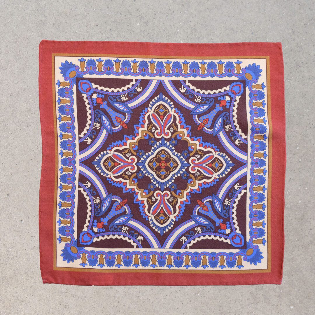 A square scarf with an intricate design in blue, red and white.