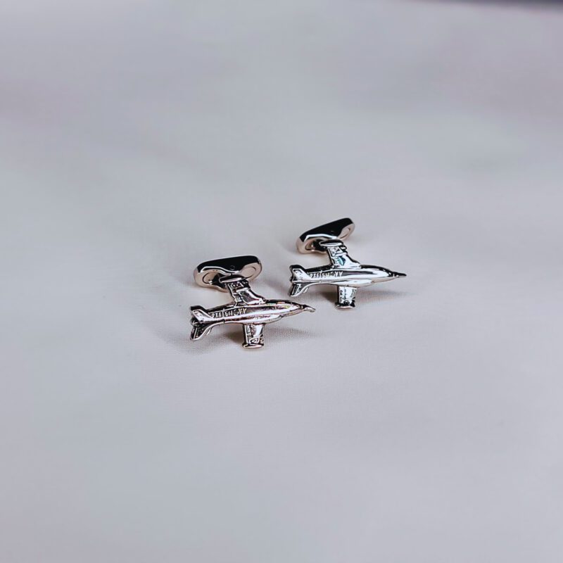 A pair of silver airplane cufflinks on top of a table.