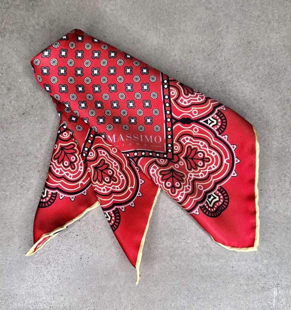 A red and black patterned scarf laying on the ground.