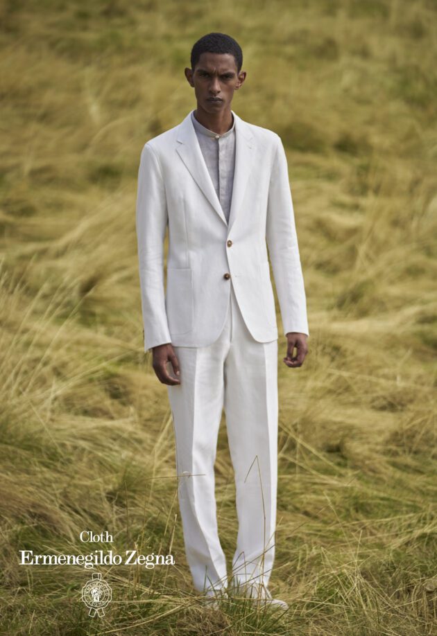 A man in white suit standing on top of a grass covered field.