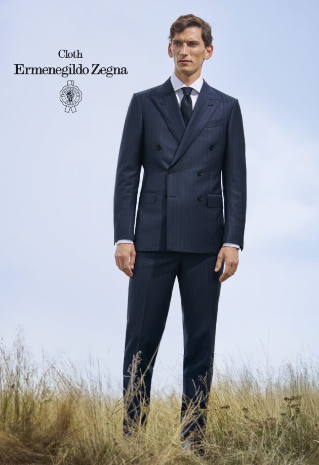 A man in suit and tie standing on top of a grass covered field.