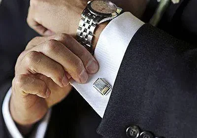 A man in a suit and tie fixing his cuff.